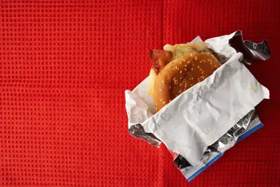 Hamburguesa envuelta en papel antigrasa de aluminio sobre un mantel rojo