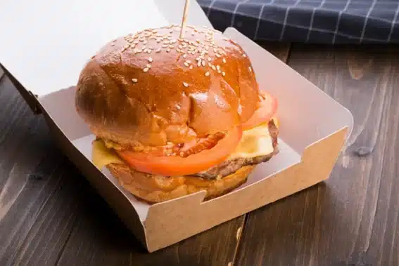 Hamburguesa con queso y tomate en un estuche de cartón kraft para llevar