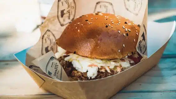 Hamburguesa gourmet de carne desmigada en una bandeja de cartón kraft con papel antigrasa impreso