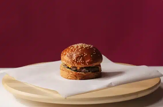 Hamburguesa gourmet con sésamo sobre papel blanco en una tabla de madera con fondo granate