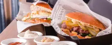 Hamburguesas gourmet en cajas negras con papel antigrasa estampado y salseros de cartón para delivery