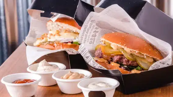 Hamburguesas gourmet en cajas negras con papel antigrasa estampado y salseros de cart&oacute;n para delivery