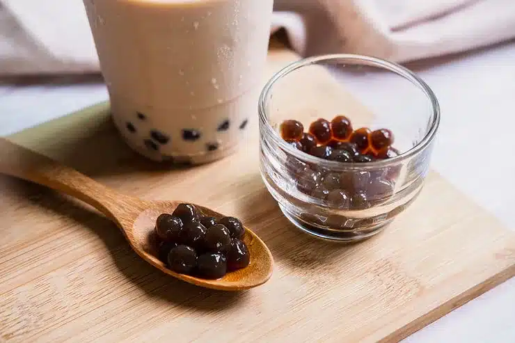 Perlas de tapioca en una cuchara de madera y un cuenco de cristal junto a un vaso de bubble tea con leche