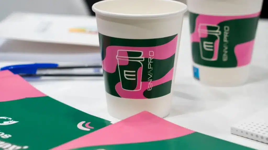 Vasos de cartón con el logotipo del vaso de Envapro sobre fondo rosa y verde