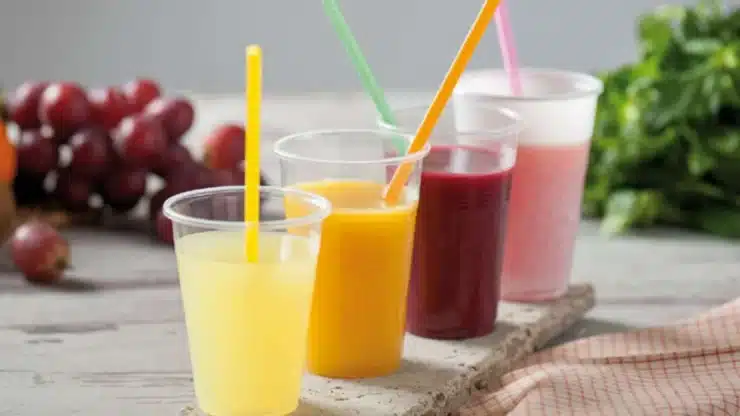 Vasos de pl&aacute;stico transparentes con zumos de colores y pajitas junto a uvas y hierbas frescas